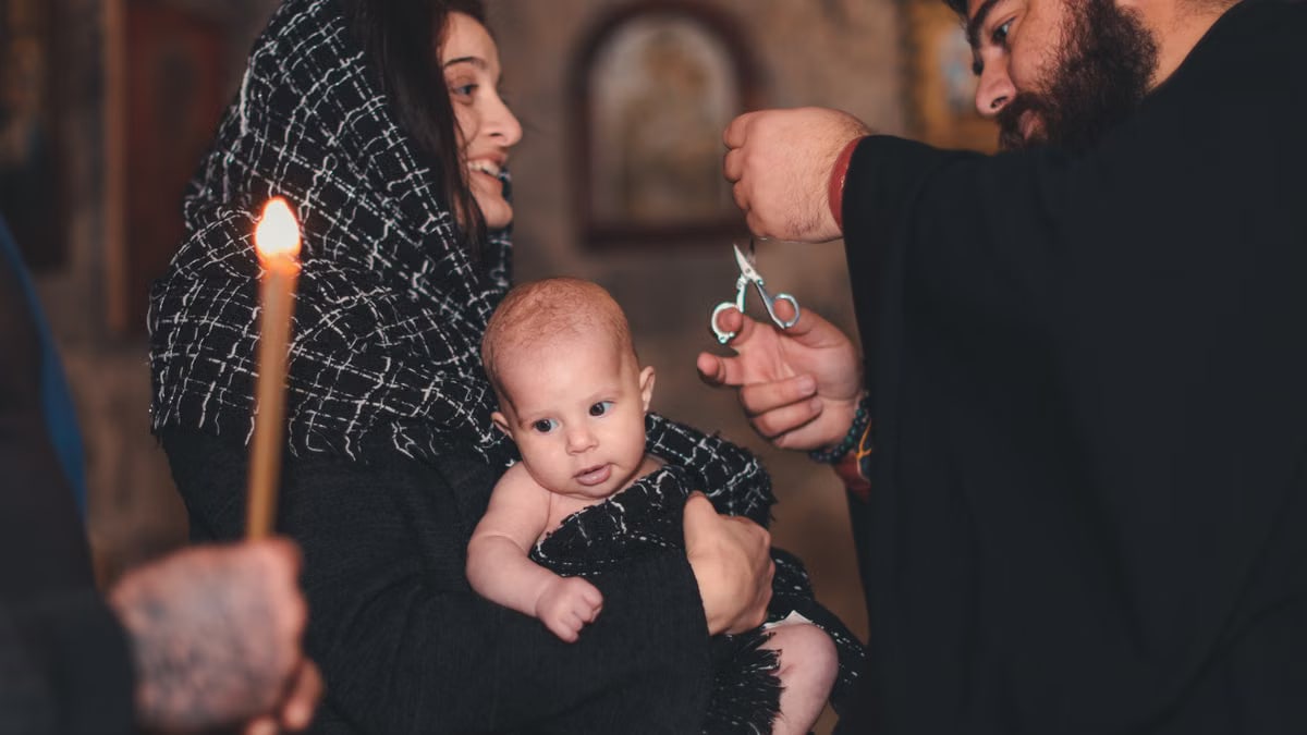An intimate Orthodox baptism ceremony featuring a priest and family with candle.