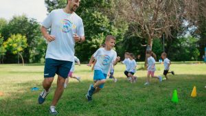 A group of kids running with an instructor during outdoor sports activities on a sunny day in a park.